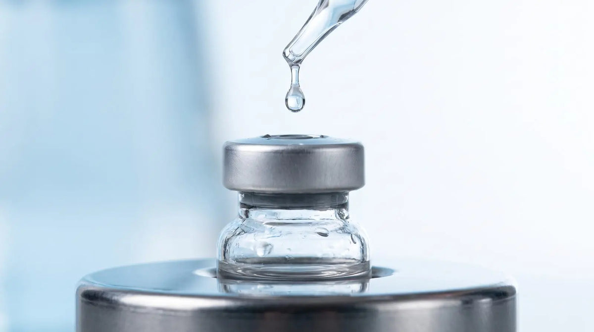 Clear laboratory vial with a droplet of reconstitution solvent from a pipette, cool blue background