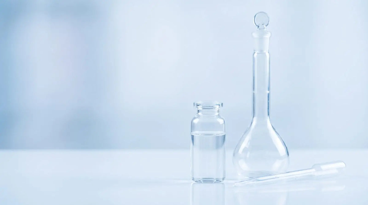 Clear glass vial beside a volumetric flask and glass pipette on a cool blue laboratory bench, representing 10 mg vial stock concentration math for research.