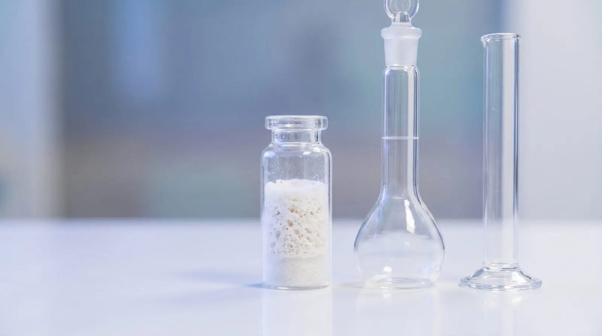 Lyophilized peptide vial beside a glass volumetric flask and graduated cylinder on a white lab bench, representing tesamorelin stock concentration calculations.