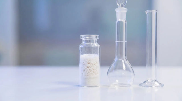 Lyophilized peptide vial beside a glass volumetric flask and graduated cylinder on a white lab bench, representing tesamorelin stock concentration calculations.